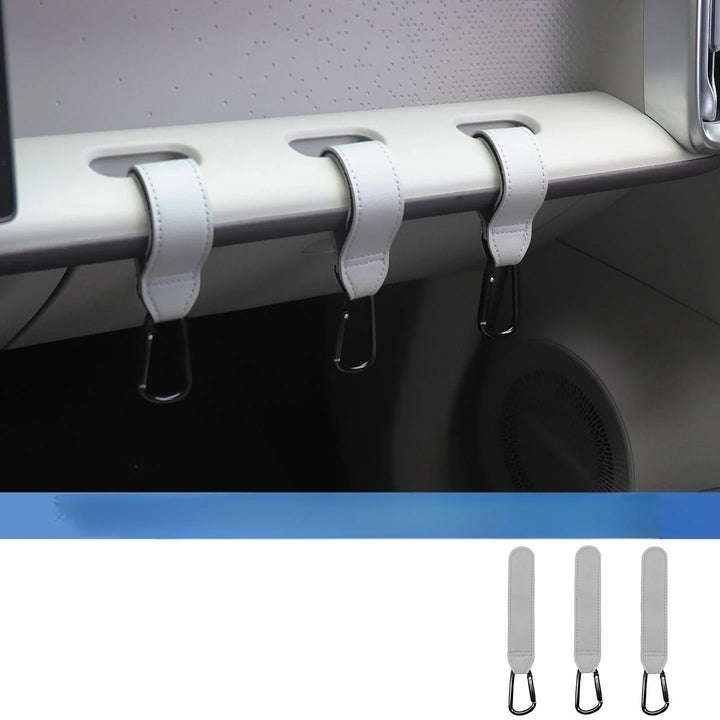Three white leather car interior hook organizers installed on a vehicle dashboard