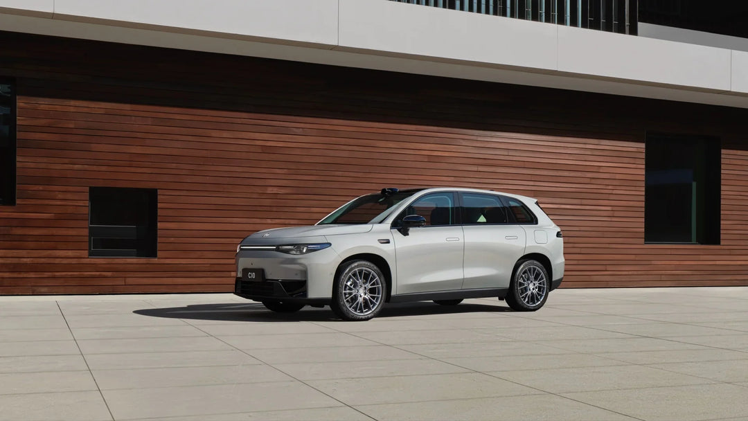 Side view of a silver Leapmotor C10 electric SUV parked in front of a modern wood-paneled building